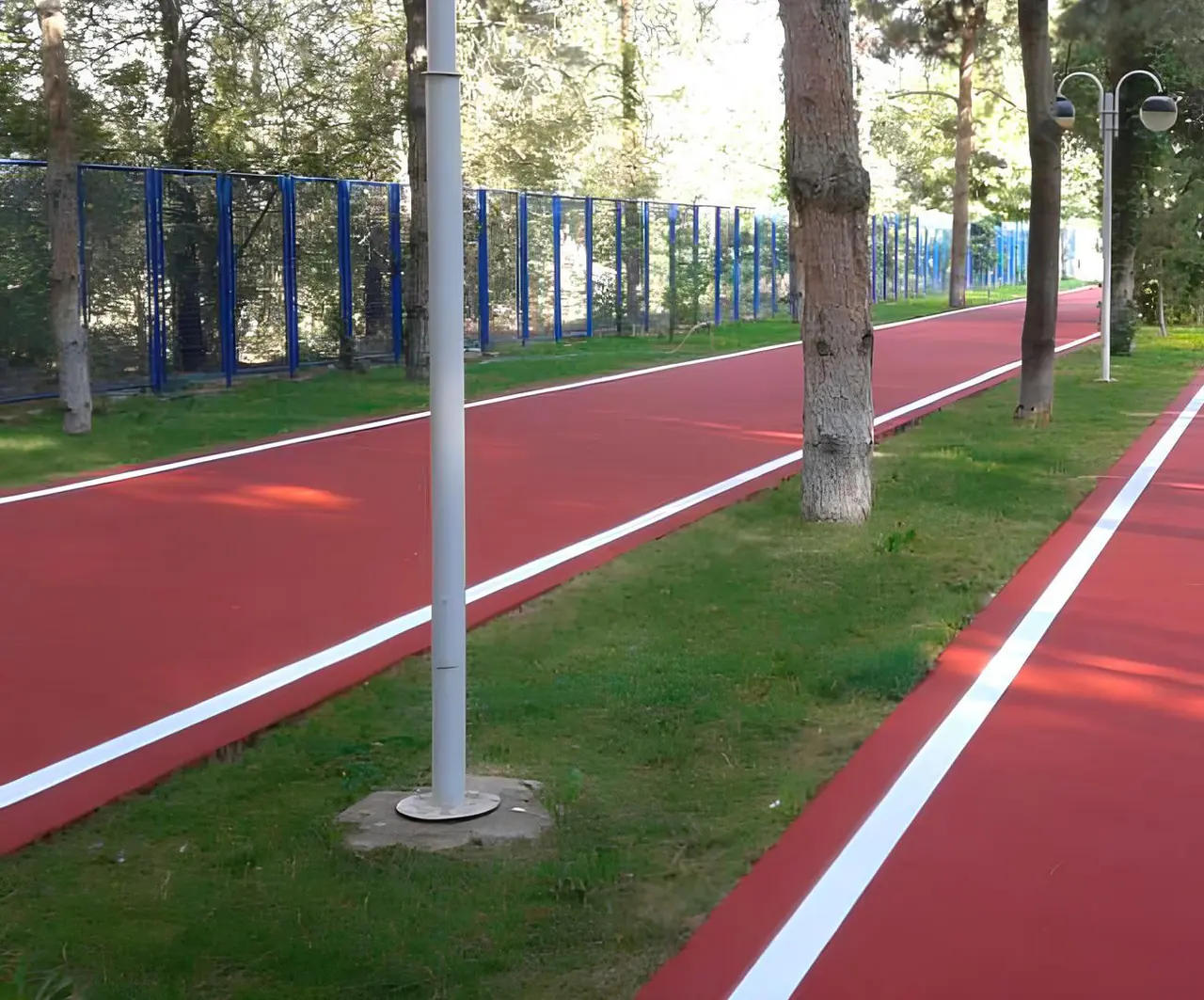Park içinde iki şeritli EPDM yürüyüş parkuru, ağaçlar ve mavi çit