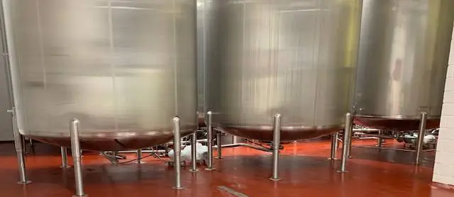 Süt veya içecek tesisinde sıra hâlinde duran büyük paslanmaz tanklar