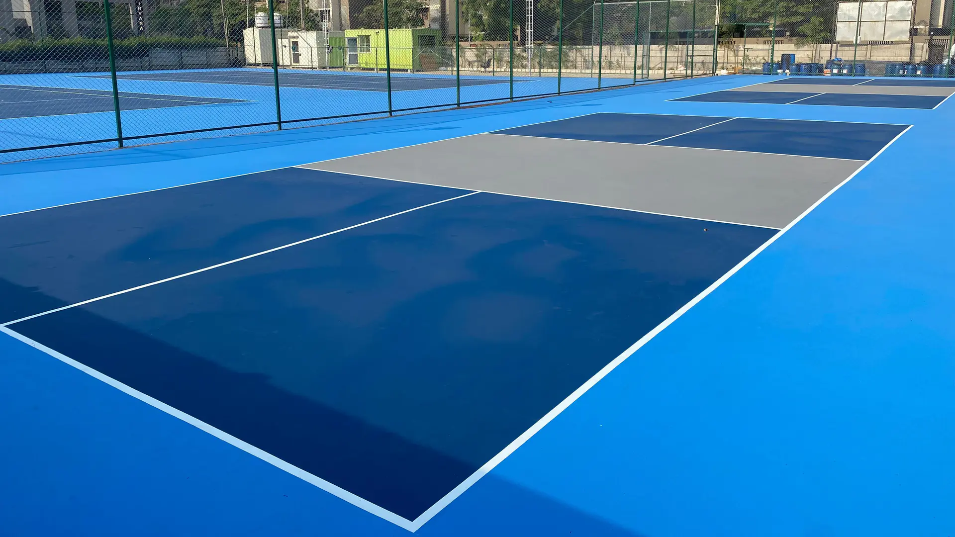 Akrilik kaplı açık tenis kortunda mavi oyun alanı, lacivert dış saha ve beyaz çizgi boyası