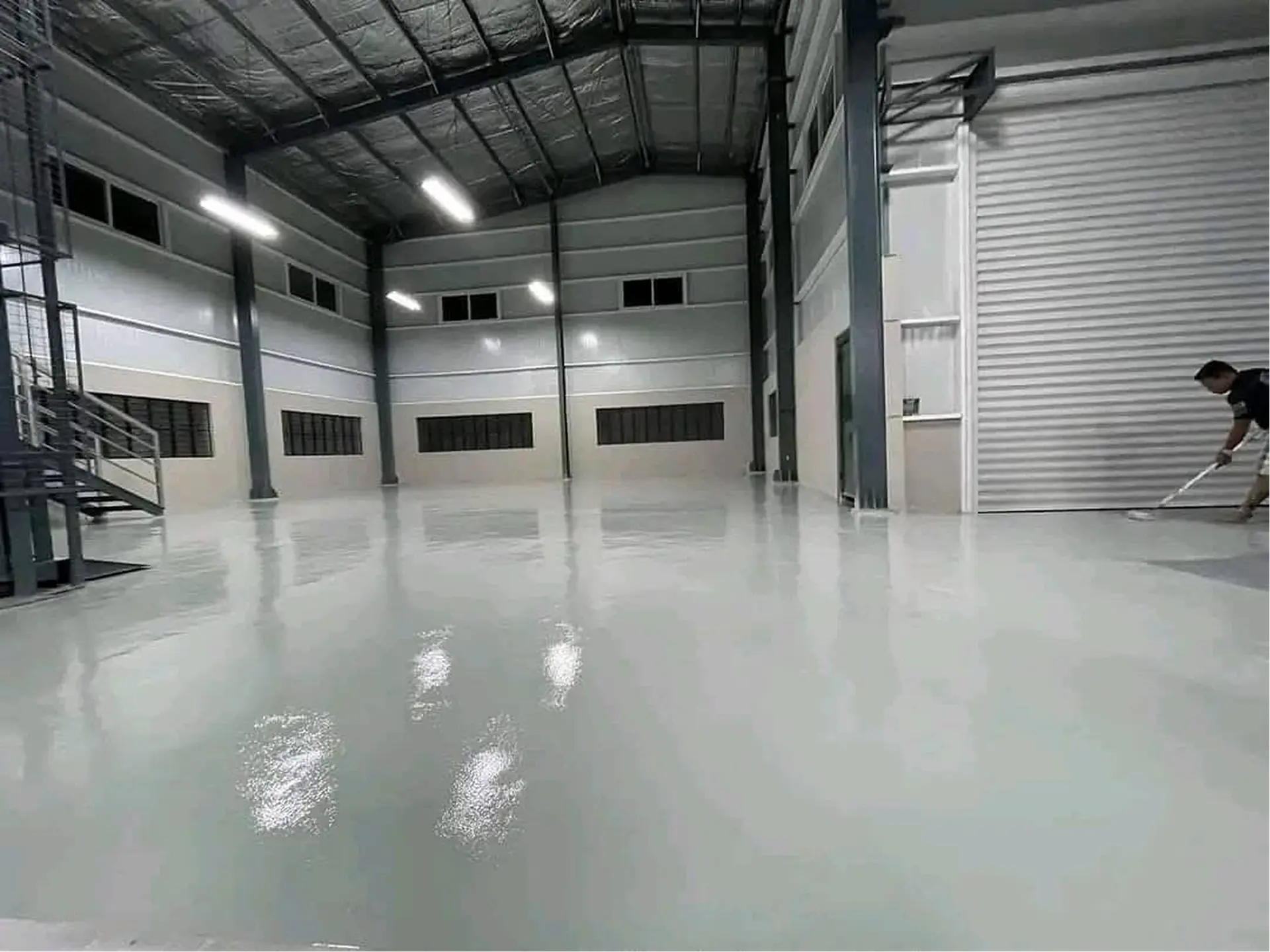 Depo zemininde gri epoksi kaplamanın rakle ile yayıldığı uygulama anı